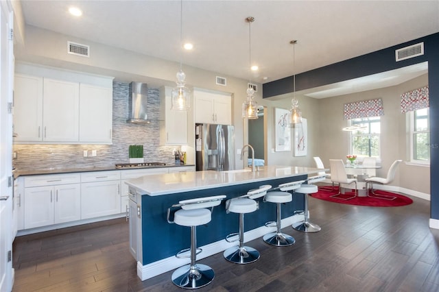 kitchen featuring appliances with stainless steel finishes, wall chimney exhaust hood, a kitchen island with sink, and dark wood-type flooring