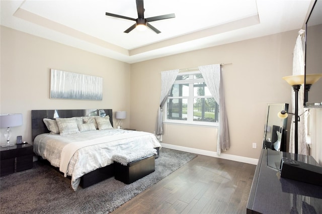 bedroom with a tray ceiling, dark wood-type flooring, and ceiling fan