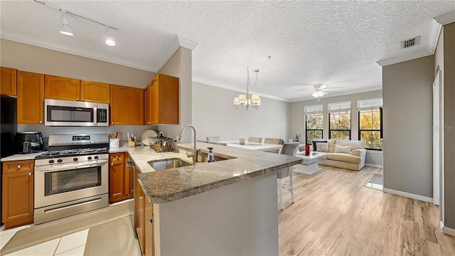 2717 Via Cipriani Unit 622B, Clearwater, FL 33764 - kitchen with stainless steel appliances, a sink, ornamental molding, a peninsula, and brown cabinetry