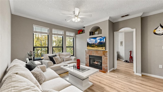 living room featuring a tiled fireplace, ceiling fan, a textured ceiling, light hardwood / wood-style floors, and crown molding