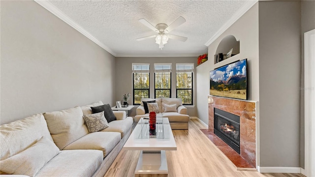 living room featuring ceiling fan, a textured ceiling, ornamental molding, and light wood-type flooring