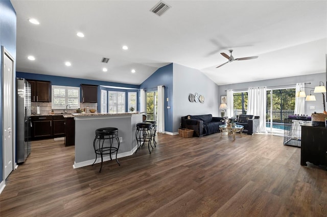 kitchen with a kitchen breakfast bar, dark brown cabinetry, vaulted ceiling, stainless steel refrigerator, and dark hardwood / wood-style floors