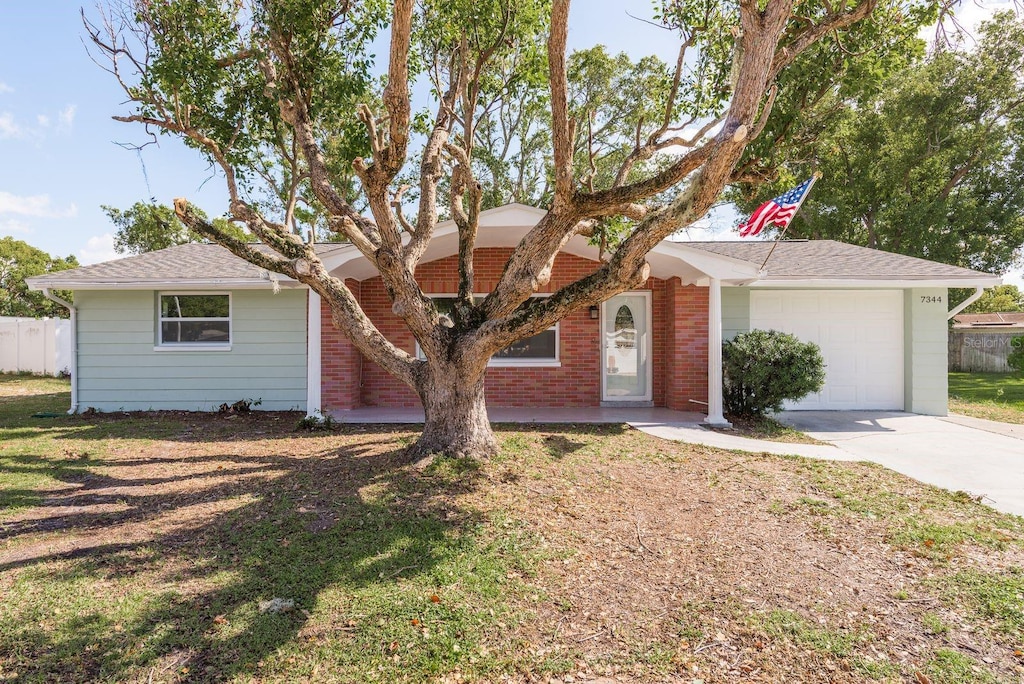 7344 Live Oak Ln, New Port Richey, FL 34653 - ranch-style home with brick siding, an attached garage, concrete driveway, and fence