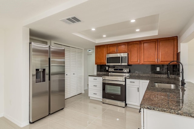 kitchen with appliances with stainless steel finishes, sink, dark stone countertops, backsplash, and a raised ceiling