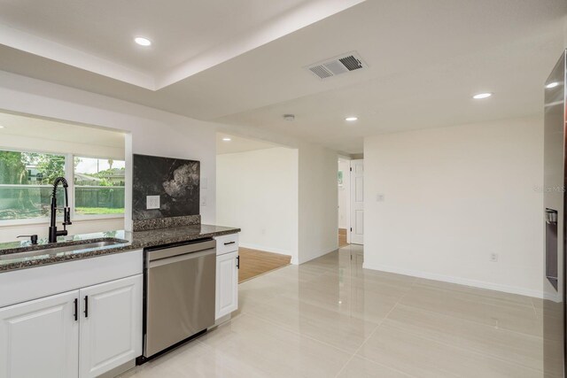 kitchen with sink, white cabinetry, stainless steel dishwasher, dark stone counters, and decorative backsplash