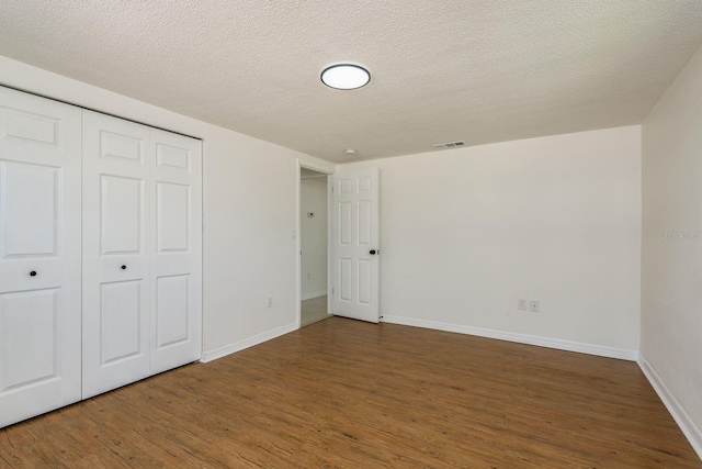 unfurnished bedroom with a textured ceiling, dark hardwood / wood-style flooring, and a closet