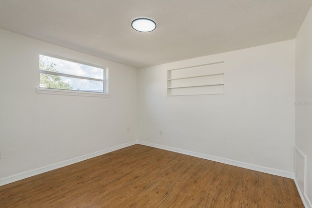 unfurnished room featuring wood-type flooring, built in features, and a textured ceiling