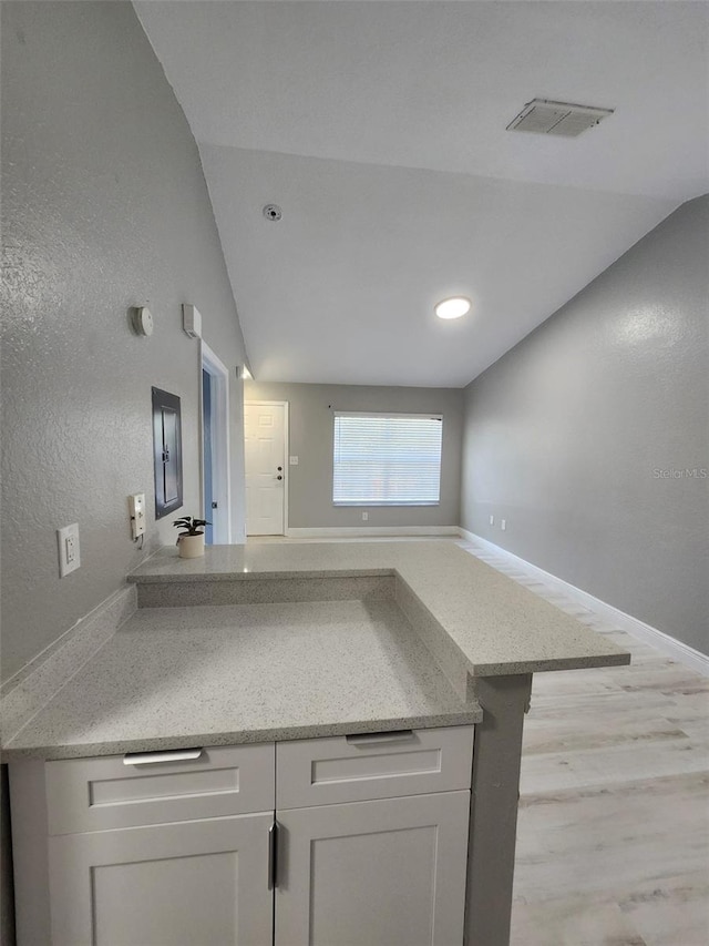 kitchen with lofted ceiling, white cabinets, light wood-type flooring, and kitchen peninsula