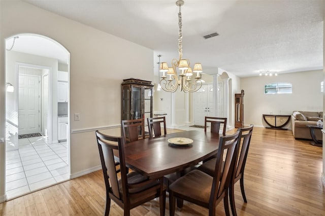 dining room with a textured ceiling, light hardwood / wood-style floors, a chandelier, and ornate columns