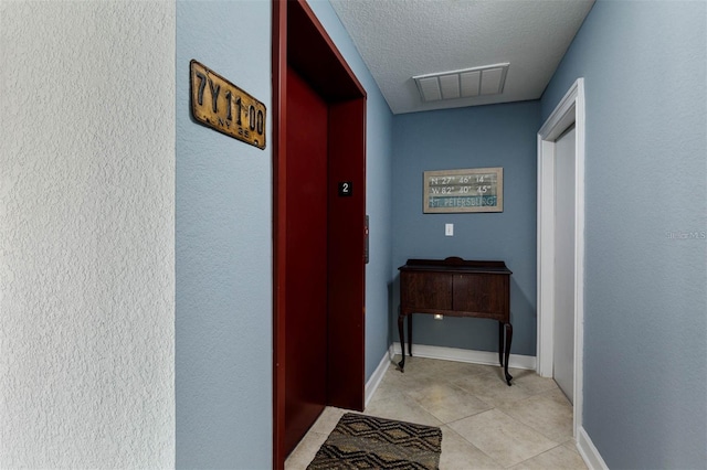 hallway with a textured ceiling and light tile patterned flooring