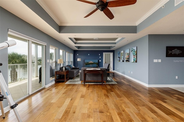 living room with ceiling fan, ornamental molding, a tray ceiling, and light wood-type flooring