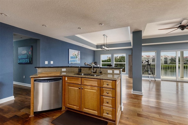 kitchen featuring light stone countertops, hardwood / wood-style flooring, stainless steel dishwasher, pendant lighting, and sink