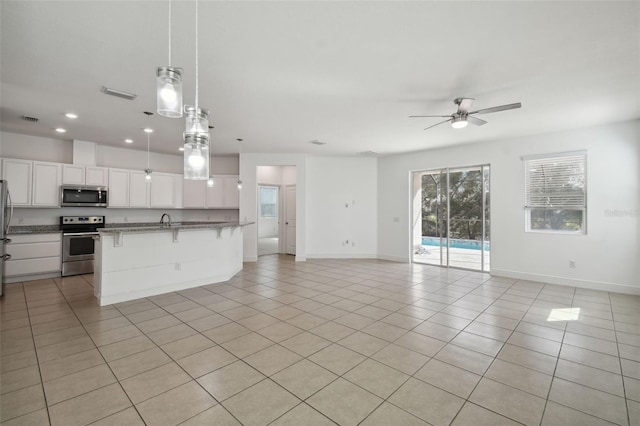 kitchen featuring white cabinets, light tile patterned floors, appliances with stainless steel finishes, decorative light fixtures, and a kitchen bar