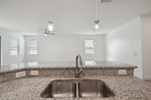 kitchen with ceiling fan, sink, light stone counters, hardwood / wood-style floors, and decorative light fixtures