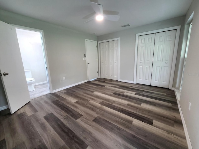 unfurnished bedroom featuring ceiling fan, ensuite bath, multiple closets, and dark hardwood / wood-style flooring