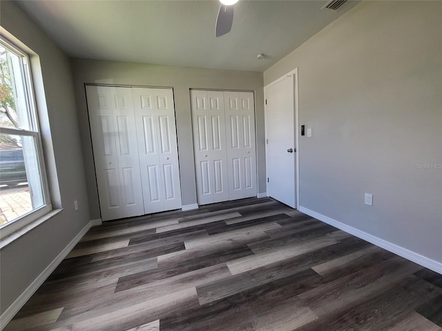 unfurnished bedroom with dark wood-type flooring, ceiling fan, and two closets