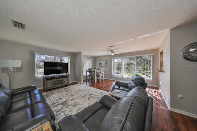 living room with a textured ceiling, ceiling fan, and dark wood-type flooring