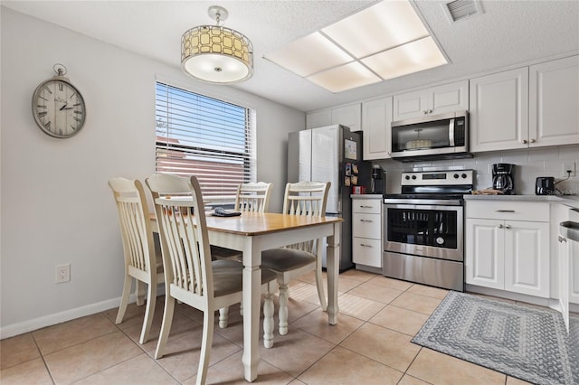 kitchen featuring stainless steel appliances, white cabinets, light tile patterned floors, backsplash, and decorative light fixtures