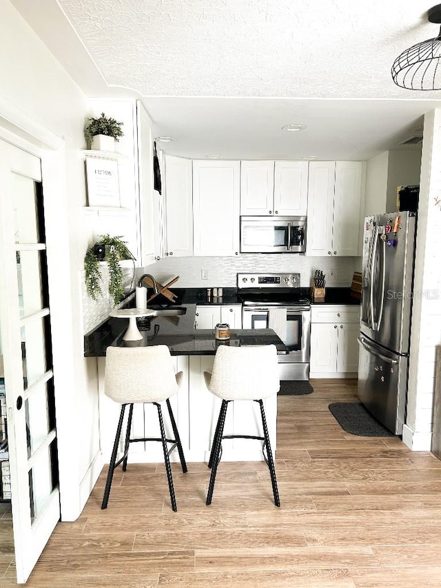 kitchen with a breakfast bar area, light hardwood / wood-style flooring, sink, white cabinets, and appliances with stainless steel finishes