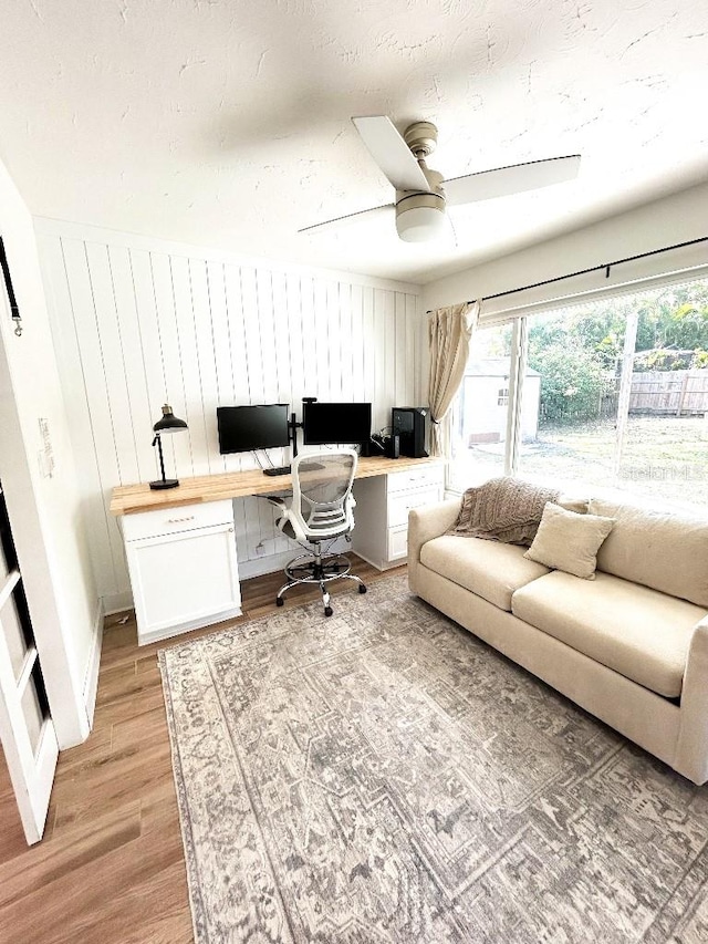 office area featuring built in desk, ceiling fan, light hardwood / wood-style flooring, and wooden walls