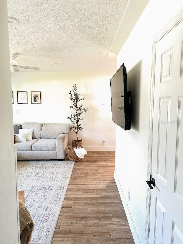 living room featuring ceiling fan, wood-type flooring, and a textured ceiling