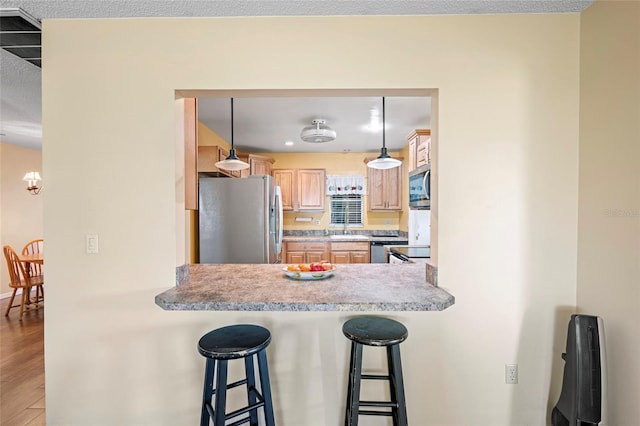 kitchen featuring light brown cabinetry, decorative light fixtures, light hardwood / wood-style floors, a kitchen bar, and stainless steel appliances