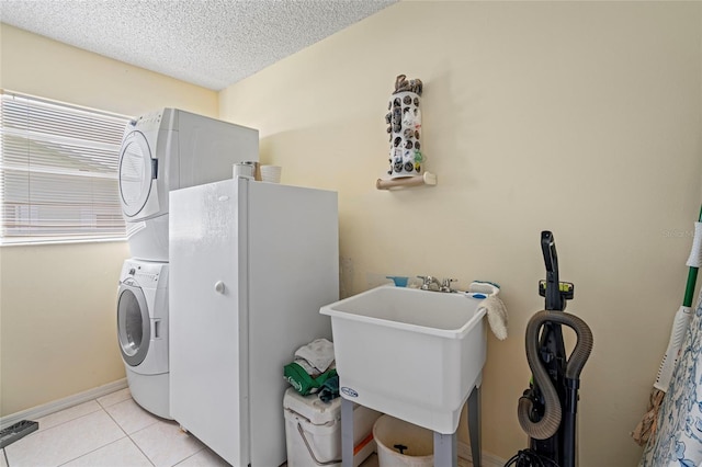 laundry area featuring a textured ceiling, sink, light tile patterned flooring, and stacked washer / drying machine