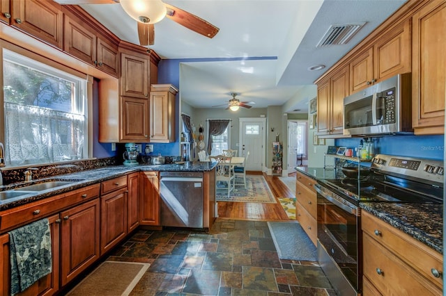 kitchen featuring sink, kitchen peninsula, stainless steel appliances, dark stone countertops, and dark hardwood / wood-style floors