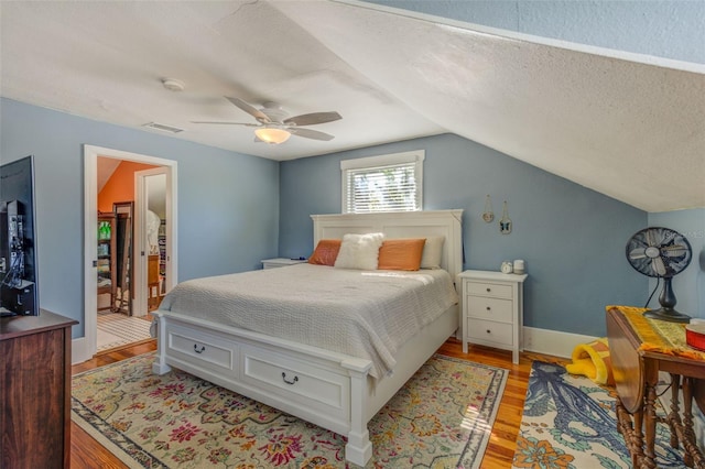 bedroom featuring light hardwood / wood-style floors, a textured ceiling, vaulted ceiling, and ceiling fan