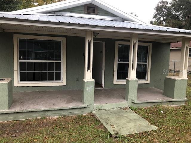 entrance to property with metal roof, a porch, and stucco siding