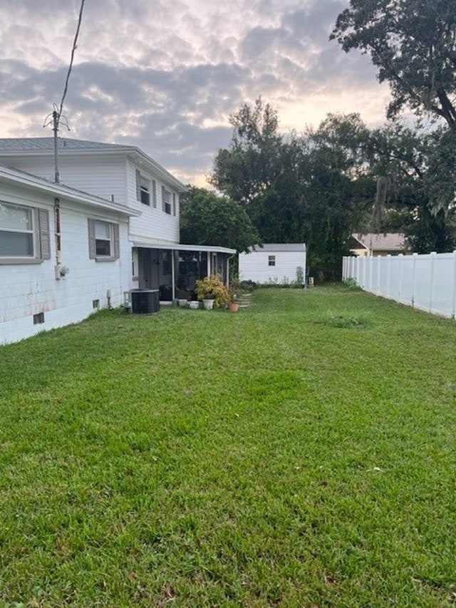 yard at dusk featuring central air condition unit and a sunroom