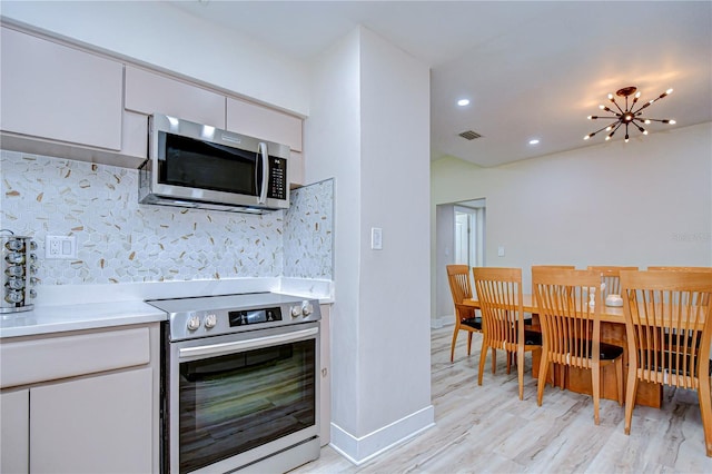 1802 E Hamilton Ave, Tampa, FL 33610 - kitchen featuring stainless steel appliances, light wood-style floors, light countertops, white cabinetry, and tasteful backsplash