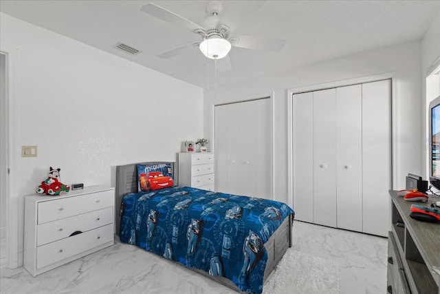 bedroom featuring ceiling fan, multiple closets, and a textured ceiling