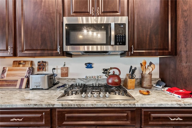 kitchen with appliances with stainless steel finishes, dark brown cabinetry, and light stone counters