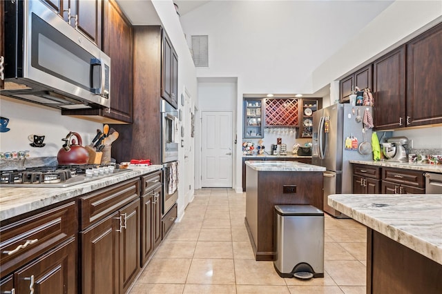 kitchen featuring dark brown cabinetry, light stone countertops, appliances with stainless steel finishes, and light tile patterned floors