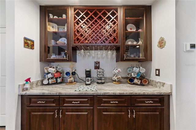 bar featuring dark brown cabinetry and light stone countertops