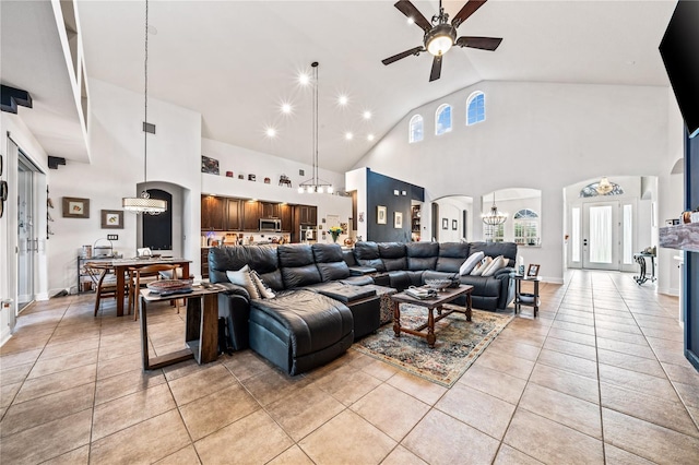 tiled living room with high vaulted ceiling and ceiling fan with notable chandelier