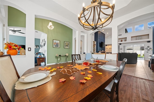 dining area featuring tile patterned flooring, ceiling fan with notable chandelier, a high ceiling, and built in shelves