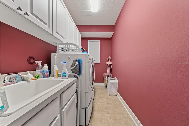 washroom with sink, light tile patterned floors, washing machine and dryer, a textured ceiling, and cabinets