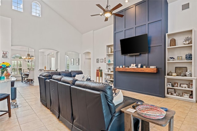 living room with high vaulted ceiling, built in shelves, ceiling fan with notable chandelier, and light tile patterned floors