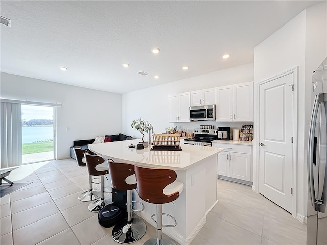 kitchen with light tile patterned flooring, an island with sink, white cabinetry, stainless steel appliances, and a breakfast bar