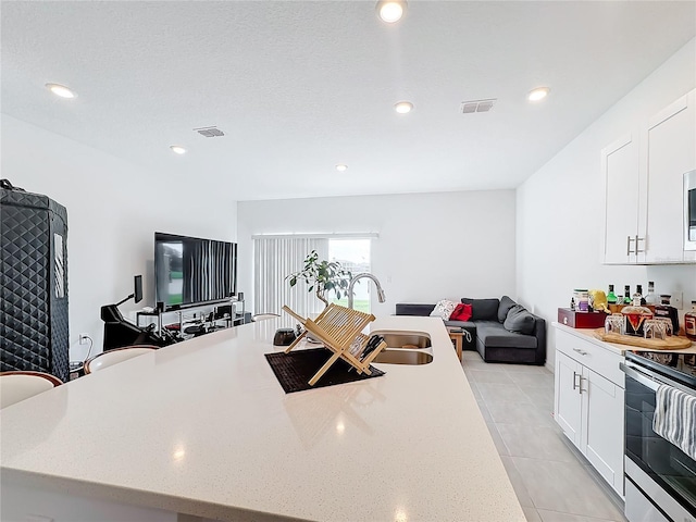 kitchen with sink, an island with sink, electric stove, white cabinets, and light tile patterned floors