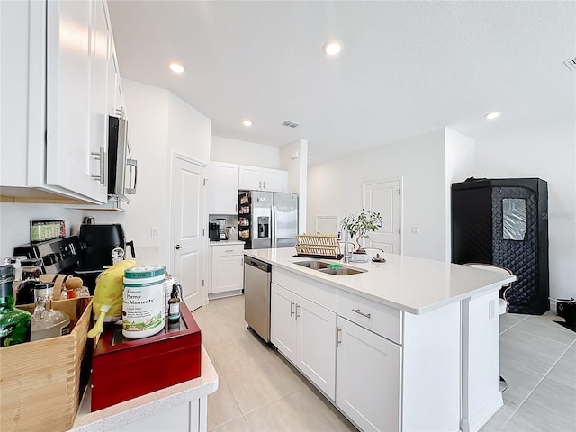 kitchen featuring an island with sink, sink, white cabinets, light tile patterned floors, and appliances with stainless steel finishes