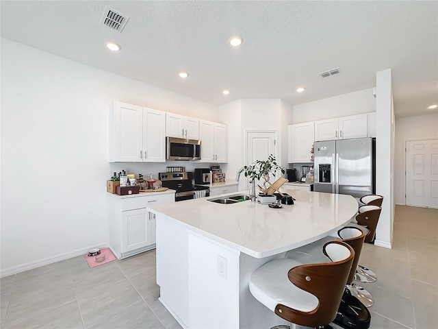 kitchen with a kitchen breakfast bar, an island with sink, sink, white cabinetry, and appliances with stainless steel finishes