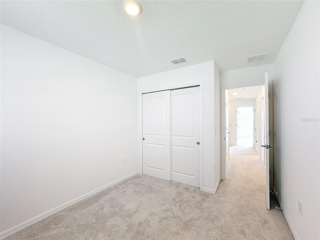 unfurnished bedroom with a closet, a textured ceiling, and light colored carpet