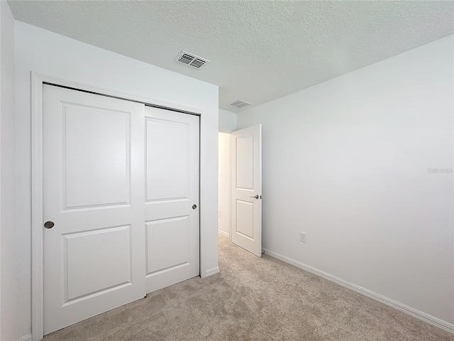 unfurnished bedroom featuring light carpet, a textured ceiling, and a closet