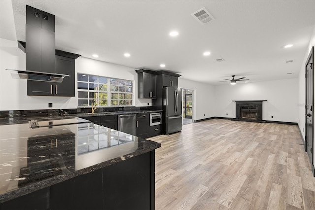 kitchen with light hardwood / wood-style flooring, stainless steel appliances, dark stone countertops, ventilation hood, and ceiling fan