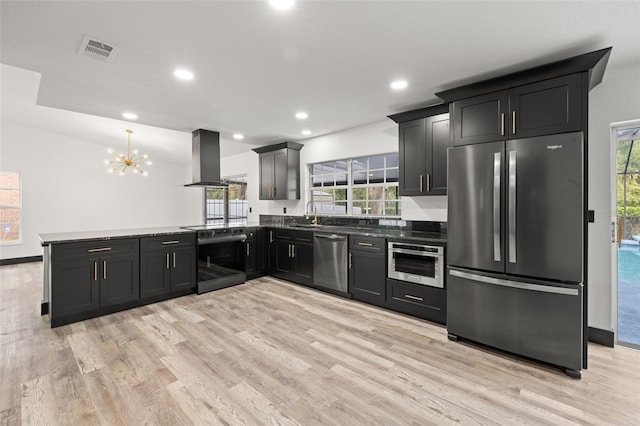 kitchen with island range hood, kitchen peninsula, decorative light fixtures, light wood-type flooring, and appliances with stainless steel finishes