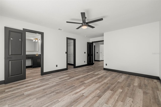 unfurnished bedroom with light hardwood / wood-style flooring, a spacious closet, connected bathroom, and ceiling fan with notable chandelier