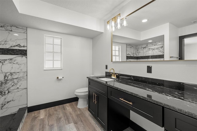 bathroom with toilet, a tile shower, vanity, and wood-type flooring